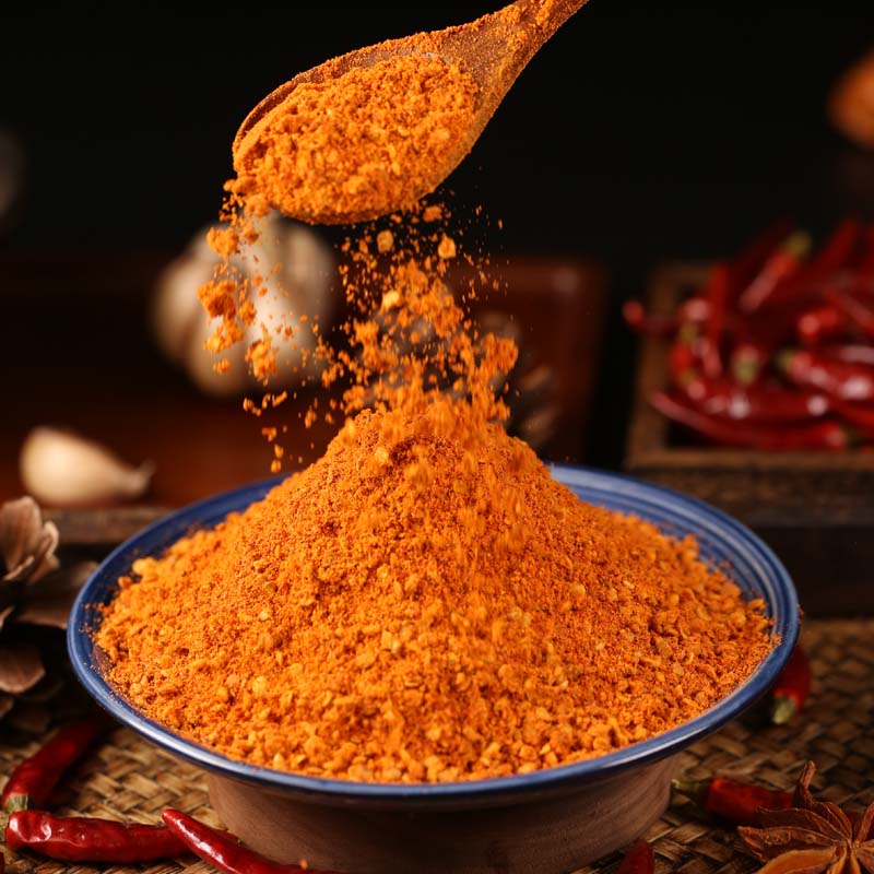 Five-spice chili dipping seasoning poured from a wooden spoon into a blue bowl