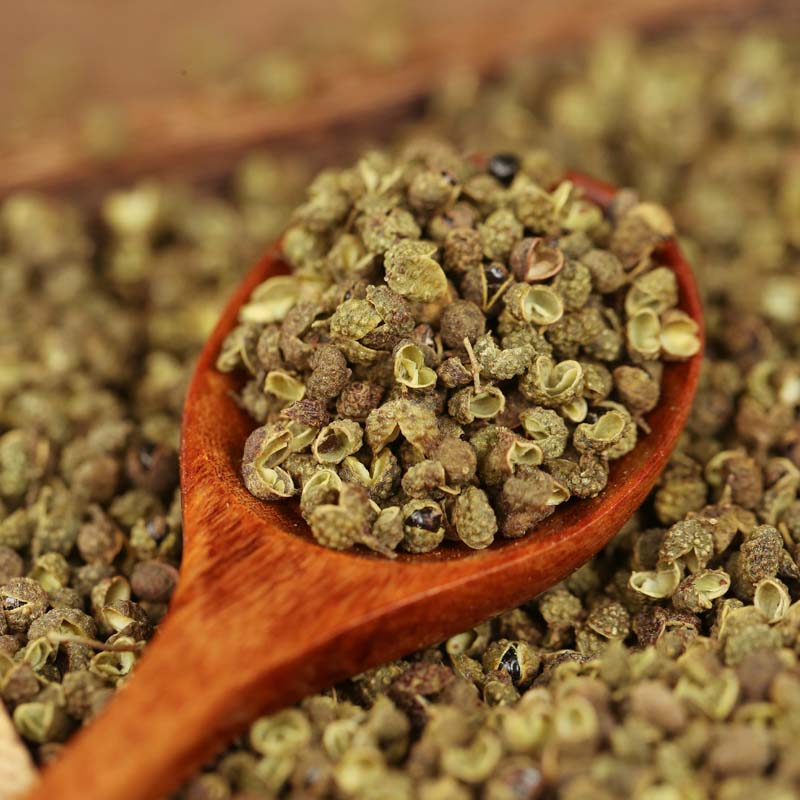 Green Sichuan peppercorns on a wooden spoon