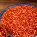 Super hot coarse chili powder filling a blue-rimmed bowl, seeds and flakes visible