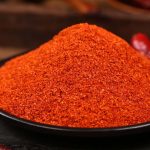 Super hot fine chili powder on a black plate with a whole dried chili pepper