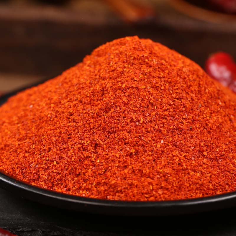 Super hot fine chili powder on a black plate with a whole dried chili pepper