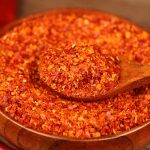 Super hot coarse chili powder lifted on a wooden spoon from a wooden bowl