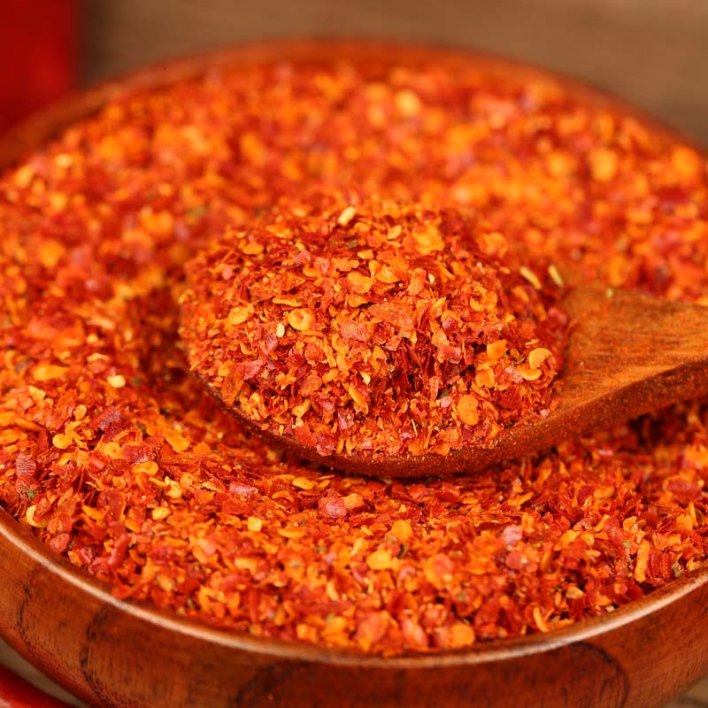 Super hot coarse chili powder lifted on a wooden spoon from a wooden bowl