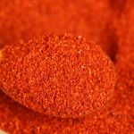 Super hot fine chili powder on a wooden spoon above a bed of ground chili