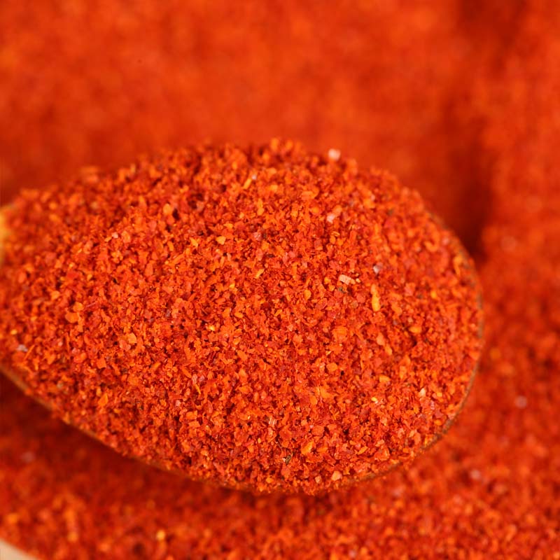 Super hot fine chili powder on a wooden spoon above a bed of ground chili