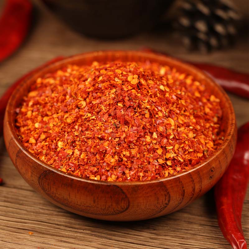 Super hot coarse chili powder in a wooden bowl beside whole dried chilies