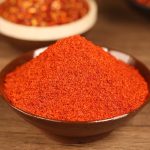 Super hot fine chili powder heaped in a dark wooden bowl on a wooden table